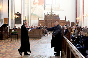 Zwei Männer gehen in einer Kirche aufeinander zu.