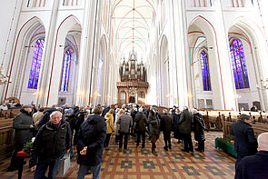 Menschen in einer Kirche. Im Hintergrund leuchten vier blaue Fenster.