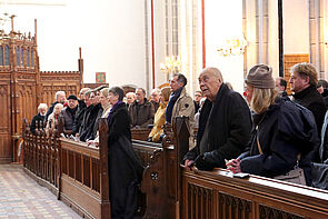 Eine voll besetzte Kirchenreihe. Ein Mann blickt hoch zu den Kirchenfenstern.