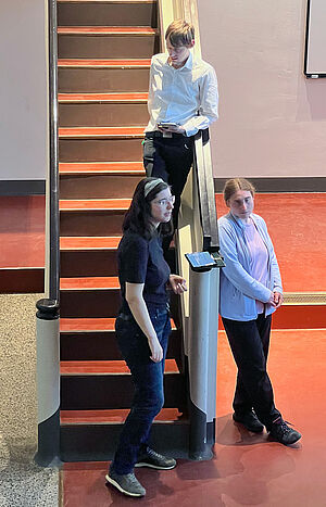 Drei junge Erwachsene stehen an einer Treppe in einem Hörsaal.