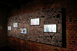 Vier Bildschirme an der Wand zeigen Filme. 