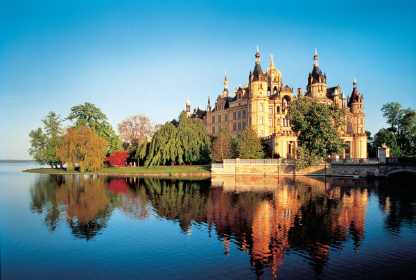 Das Schweriner Schloss umgeben von Bäumen und Wasser.