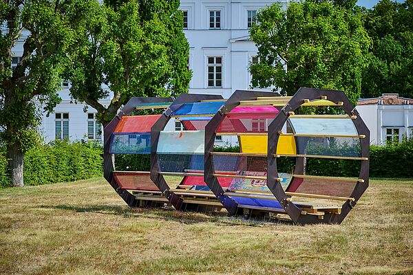 Eine Röhre mit buntem Plexiglas auf einer Wiese.