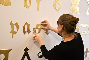 Künstlerin Susanne Gabler montiert einen Buchstaben an eine Wand.