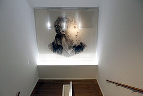Ein Porträt im Treppenaufgang hängt an der Wand und wird beleuchtet. 