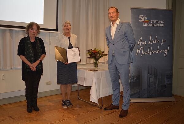 Zwei Frauen und ein Mann bei der Preisverleihung auf der Bühne.