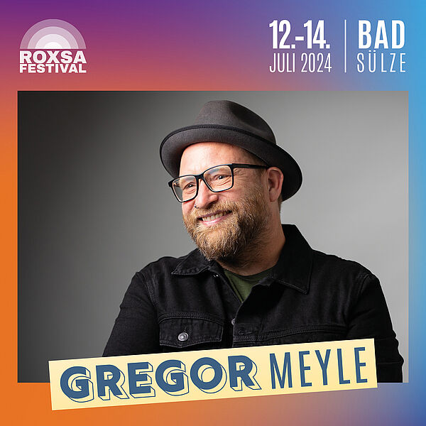 Ein Porträt von Gregor Meyle. Der Sänger trägt Hut, Brille, dunkle Sachen und lacht. 