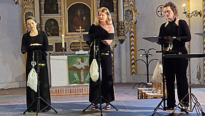 Drei Musikerinnen singen in einer Kirche.
