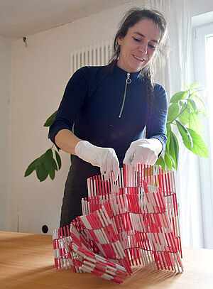 Marike Schreiber baut vor ihr auf einem Tisch ein Kunstwerk aus Fluchtstangen auf.