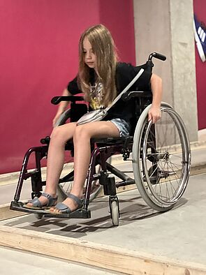 Hanna sitzt probeweise in einem Rollstuhl. Eine neue Erfahrung.