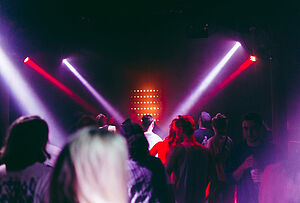 Menschen tanzen auf einer Tanzfläche. Scheinwerferlicht taucht den Raum in rote und lila Farben.