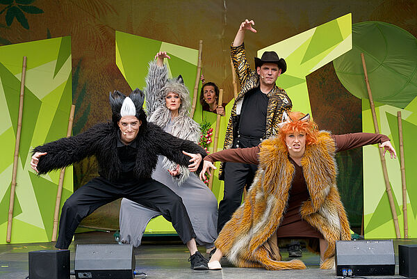 Darstellende in Kostümen des Dschungelbuchs posieren auf einer Bühne mit grünem Hintergrund.