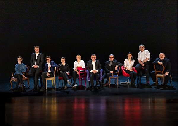 Zehn Personen sitzen auf Stühlen. Bühnenbild mit den Verantwortlichen des Staatstheaters. 