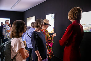 Mehrere Personen in einem abgedunkelten Raum betrachten die Ausstellungsstücke.