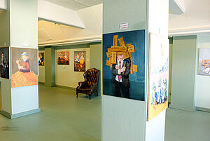 Die in grün gehaltene Ausstellungshalle. In der Mitte zwei Säulen. An den Wänden hängen die Bilder der Ausstellung.